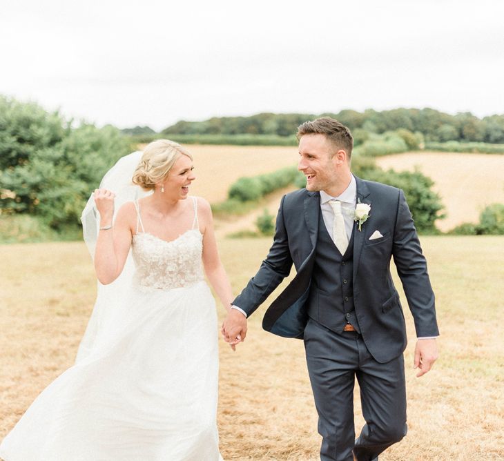 Bride in Lace Wedding Dress and Cathedral Veil and Groom in  Navy Moss Bros. Suit Laughing Together