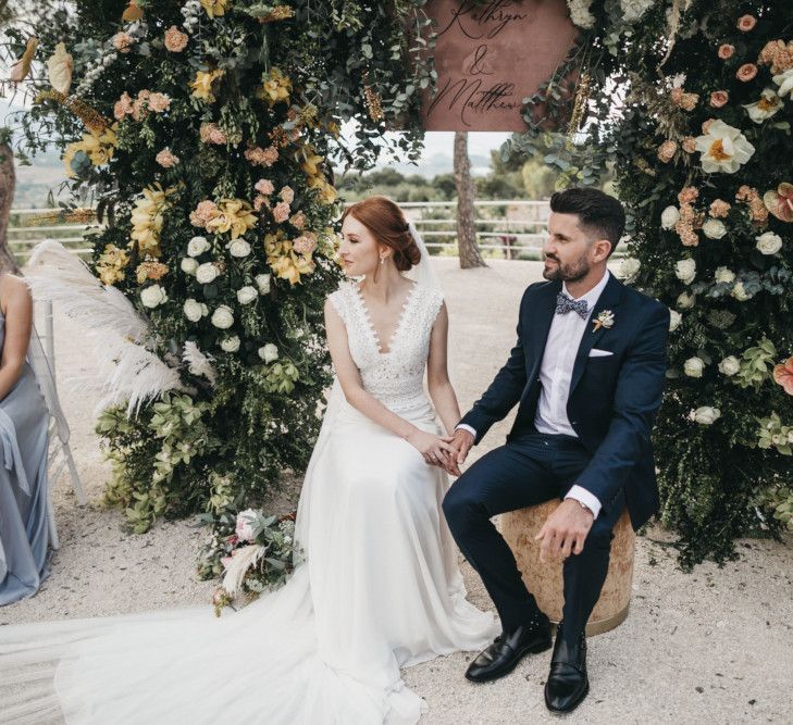 Bride and Groom Holding Hands During the Wedding Ceremony with a Floral Arch Backdrop