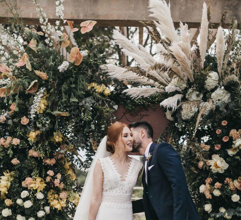 Groom in Navy Tuxedo Kissing His Bride on the Cheek During the Wedding Ceremony