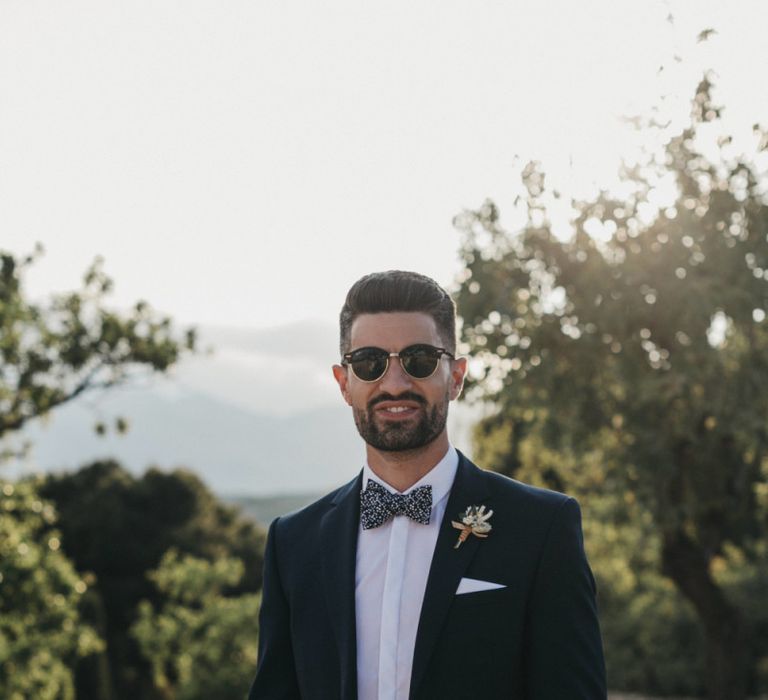 Stylish Groom in Navy Suit with Floral Bow Tie and Sunglasses