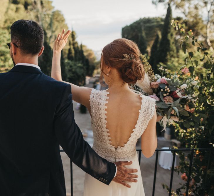 Bride in Backless Pronovias Wedding Dress and Groom in Navy Suit Waving to Their Wedding Guests on the Balcony