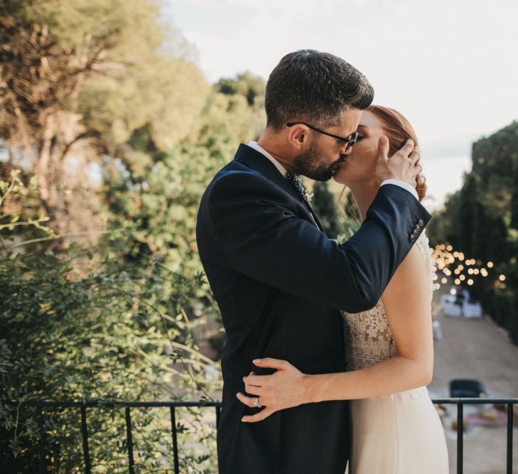 Groom in Navy Suit Kissing His Bride on the Balcony