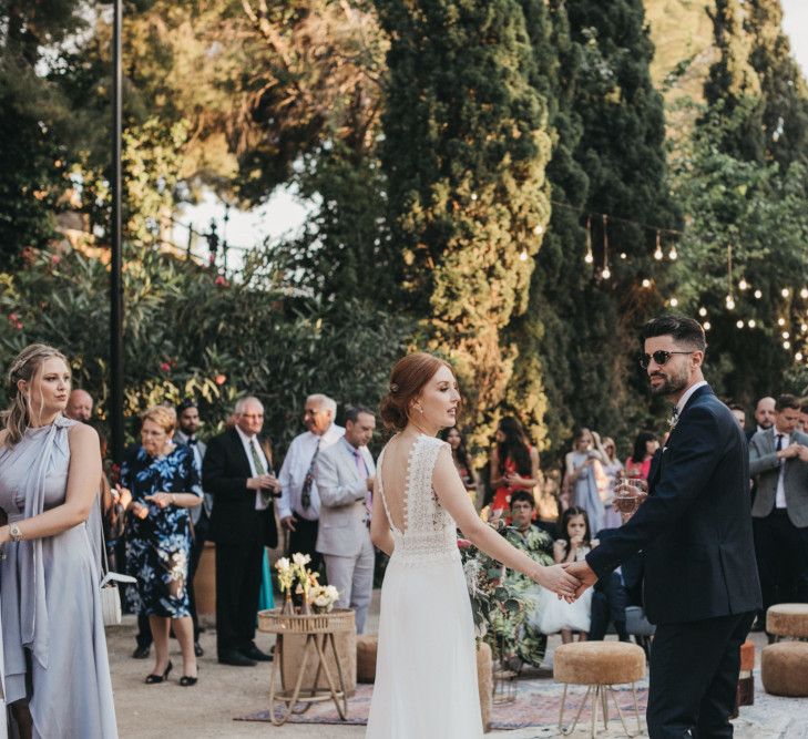 Bride in Pronovias Wedding Dress and Groom in Navy Suit Holding Hands at the Wedding Reception