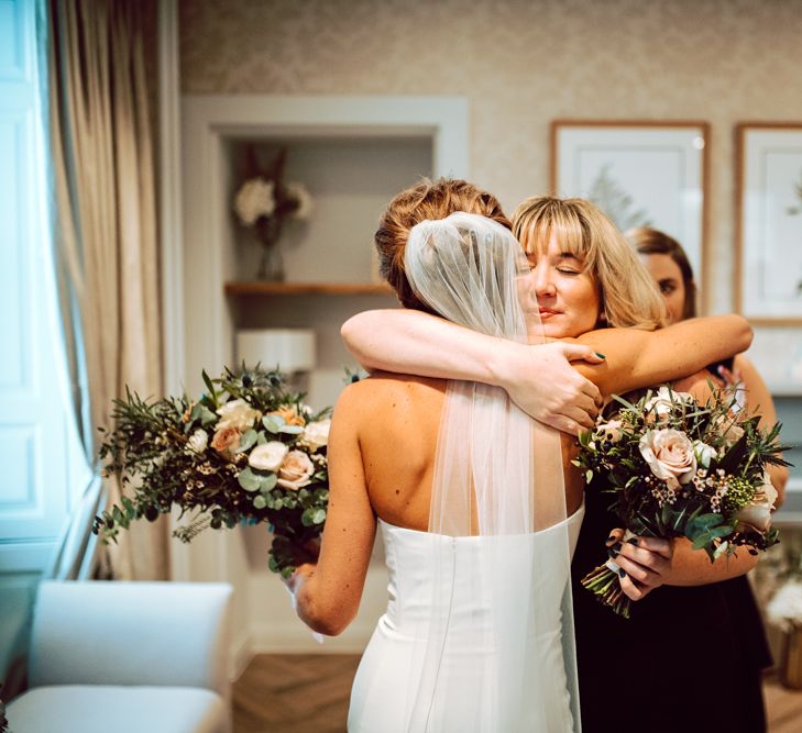 Bride in strapless wedding dress being embraced by wedding guests