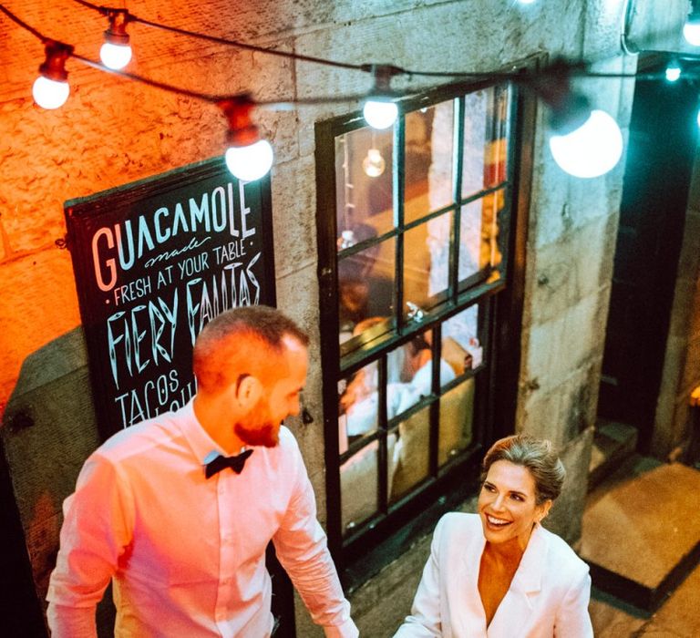 Stylish bride and groom at bar reception in a blazer evening dress