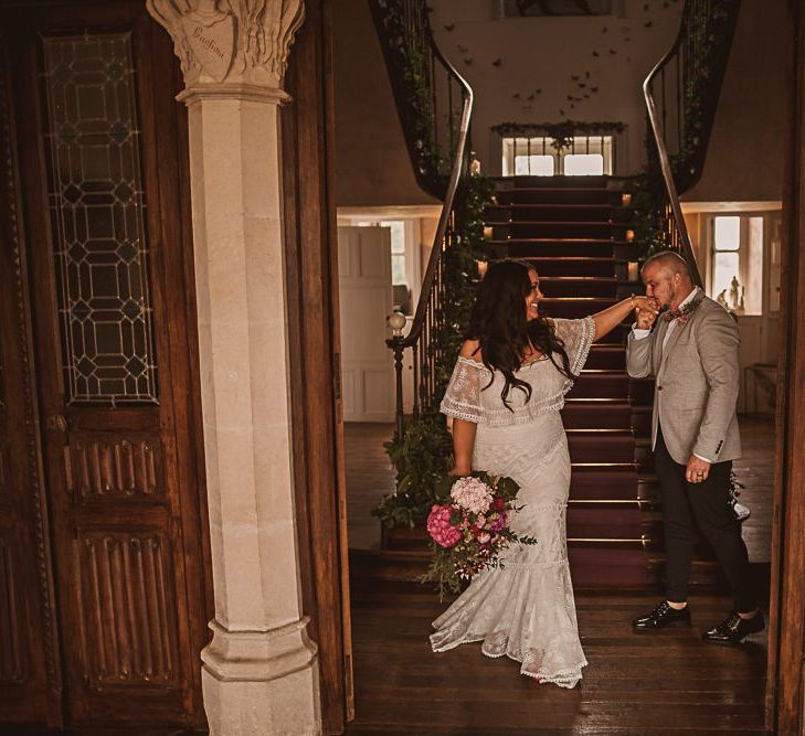 Groom in Grey Blazer and Bow Tie Kissing His Brides Hand in aGrace Loves Lace Wedding Dress