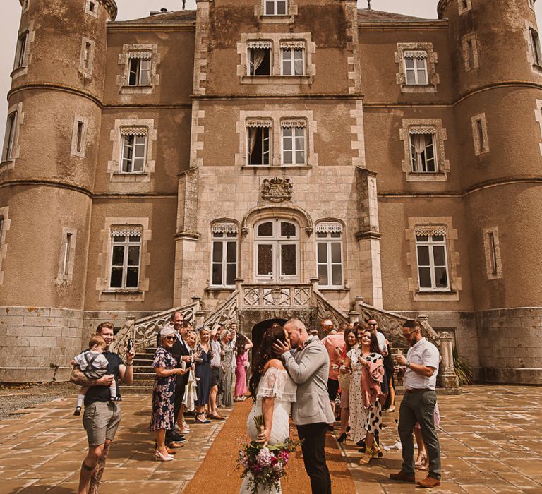 Bride in Grace Loves Lace Wedding Dress and Groom in Grey Blazer and Bow Time Kissing in Front of the French Chateau featured on escape to the chateau