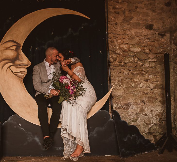 Bride in Emanuela Grace Loves Lace Wedding Dress and Groom in Grey Blazer Embracing on a Giant Moon