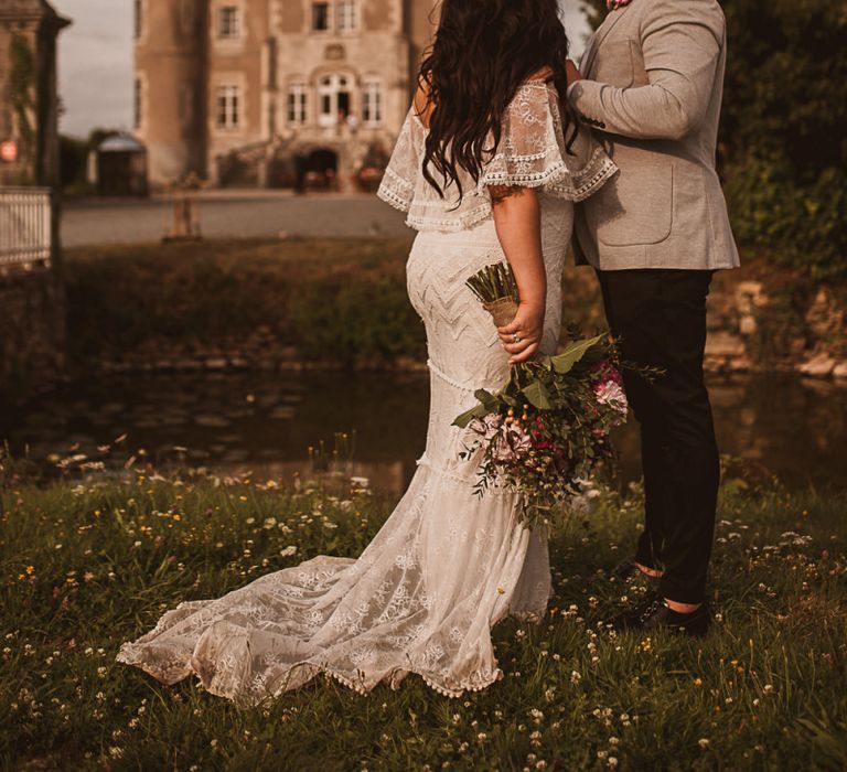 Bride in Emanuela Grace Loves Lace Wedding Dress and Groom in Grey Blazer Standing in Front of Their French Chateau Wedding Venue