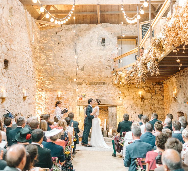 Bride in Chiffon Polka Dot Dress by Kate Halfpenny | Bridal Flower Crown | Groom in Blue Hugo Boss Suit with Dusty Blue Tie | Wedding Ceremony at Duxford Barns | Festoon Lights | Sunflower Chair Ends | Colourful Paper Cranes &amp; Sunflower Wedding Décor in Rustic Barn | Sarah-Jane Ethan Photography