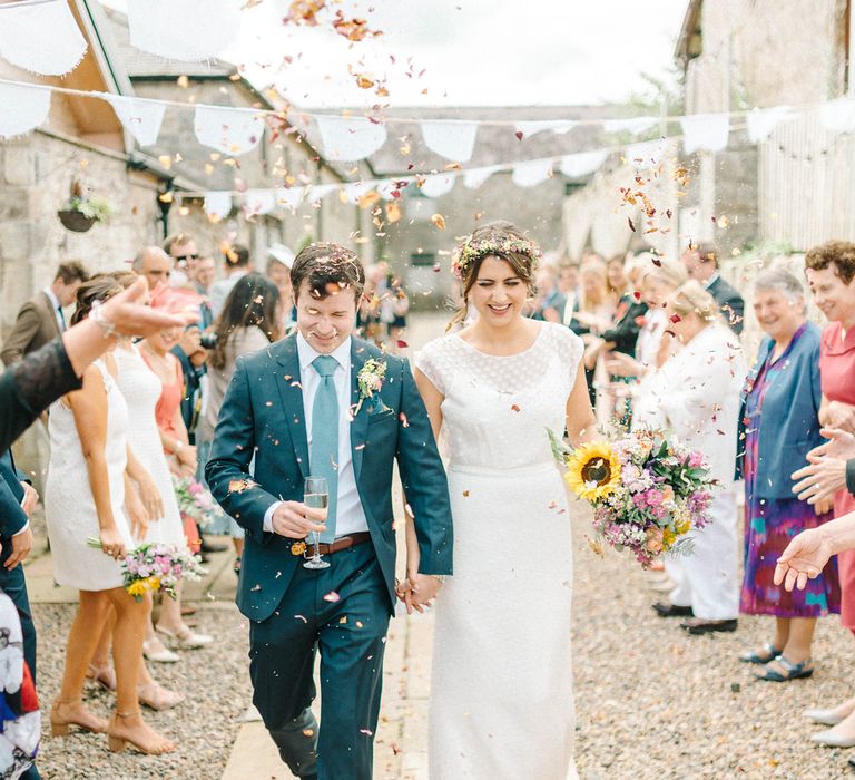 Bride in Chiffon Polka Dot Dress by Kate Halfpenny | Bridal Flower Crown | Groom in Blue Hugo Boss Suit with Dusty Blue Tie | Bright Bouquet with Sunflowers | Real Petal Confetti | White Bunting | Colourful Paper Cranes &amp; Sunflower Wedding Décor in Rustic Barn | Sarah-Jane Ethan Photography