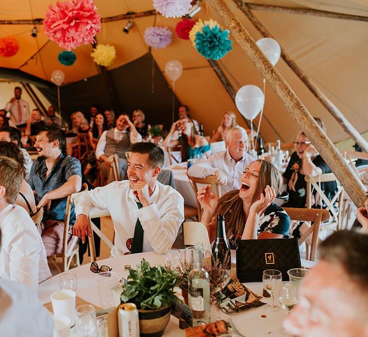 Guests enjoy wedding speeches with bright pompom decor