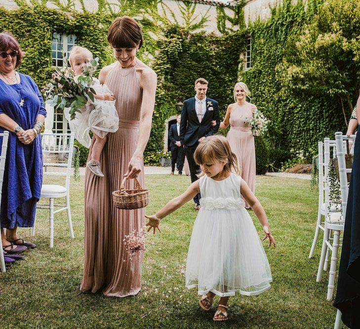 Bridesmaid in pink dress walks down the aisle with flower girls