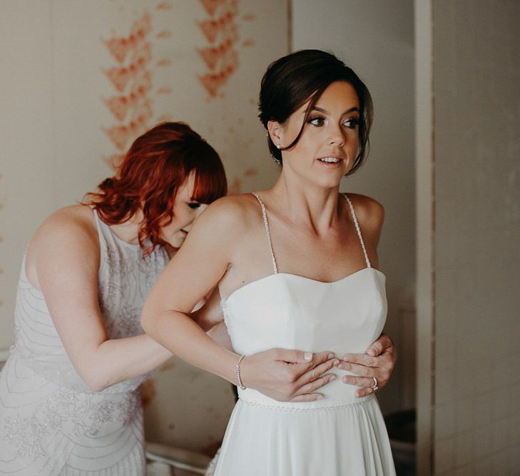 Bride getting into a thin strap bridal gown