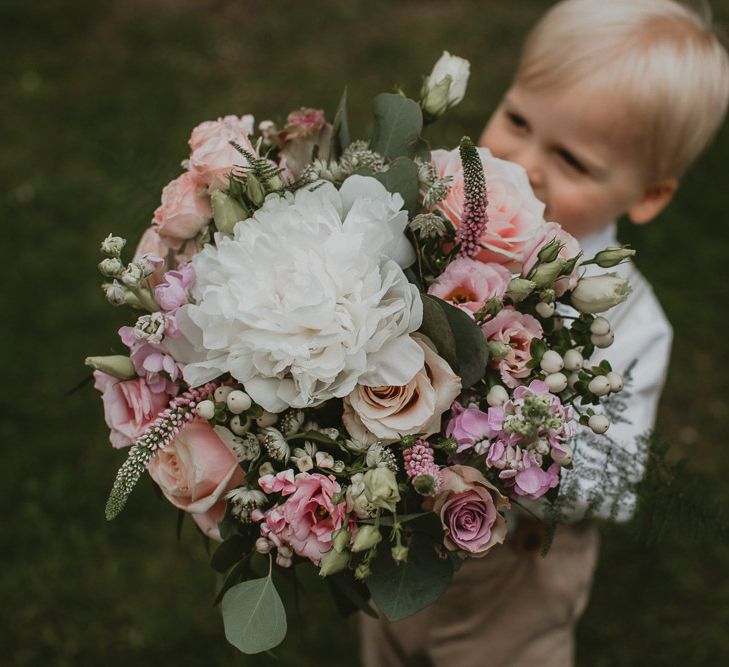 Page boy holding a spring bouquet including peonies, roses and stocks