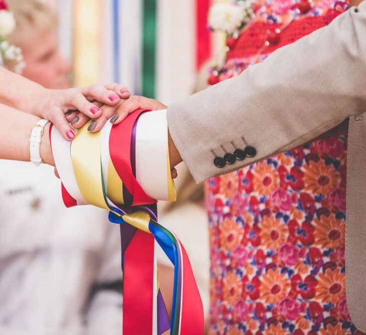 Brightly coloured ribbon hand fasting at marquee village fete themed celebration