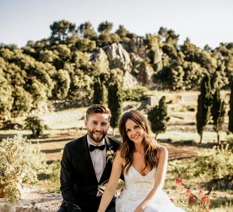 Bride in Tiered Lace Emma Beaumont Wedding Dress and Groom in Givenchy Tuxedo Sitting Hand in Hand