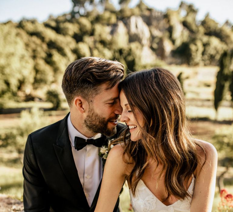 Bride in Tiered Lace Emma Beaumont Wedding Dress and Groom in Givenchy Tuxedo Sitting Embracing