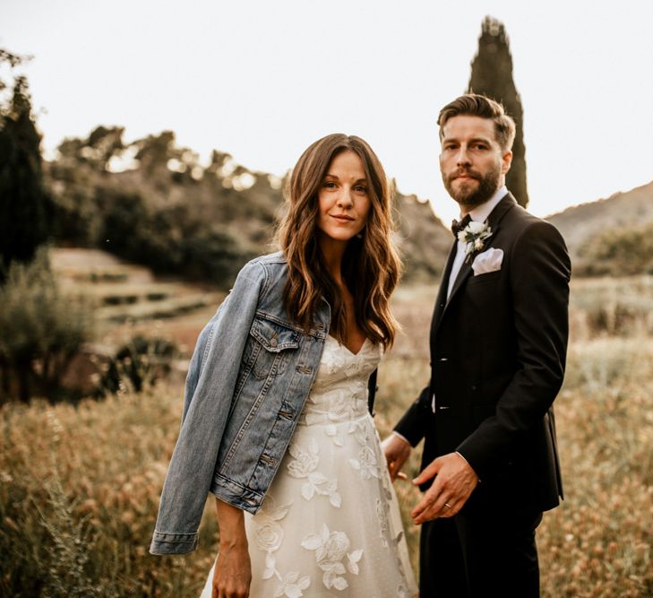 Bride in Tiered Lace Emma Beaumont Wedding Dress and Blue Denim Jacket and Groom in Givenchy Tuxedo