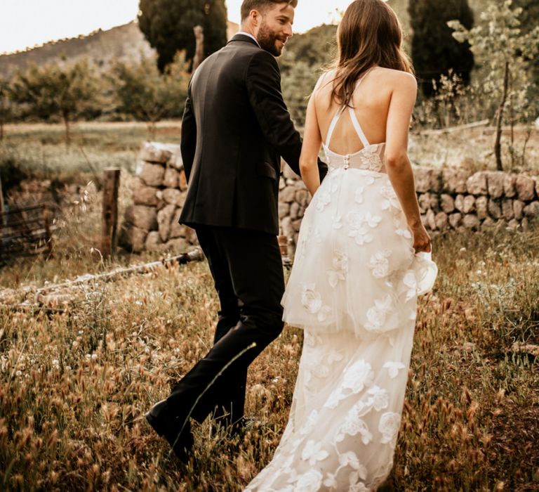 Bride in Tiered Lace Emma Beaumont Wedding Dress and Groom in Givenchy Tuxedo Walking Through Fields