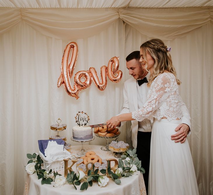 Bride and Groom Cutting the Wedding Cake with Gold Foil Love Balloon as Cake Table Backdrop