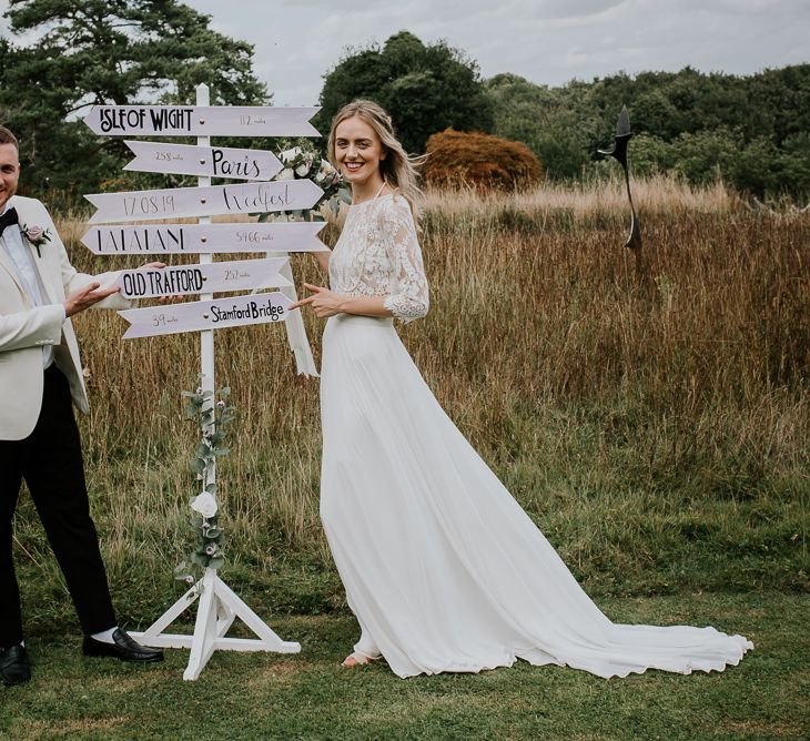 Bride in Wendy Makin Bridal Separates and Groom in White Dinner Jacket Standing Next to a Sign Post