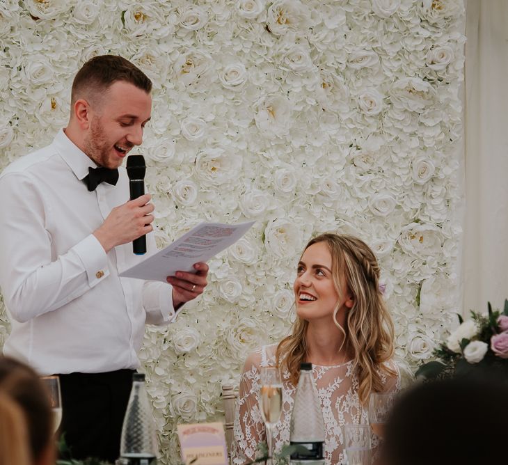 Groom in Bow Tie Giving His Wedding Speech in Front of a White Flower Backdrop