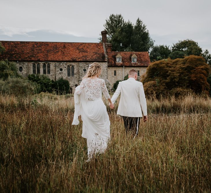 Bride in Lace Top and Plain Skirt by Wendy Makin  with Groom in White Dinner Jacket and Bow Tie  Walking Through a Field