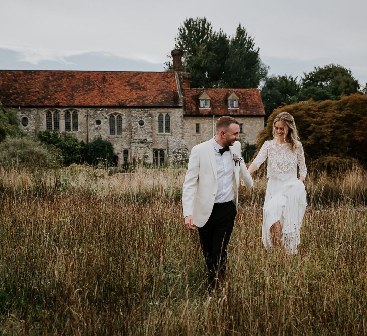 Bride in Lace Top and Plain Skirt by Wendy Makin with Groom in White Dinner Jacket and Bow Tie  Hand in Hand  in a Field