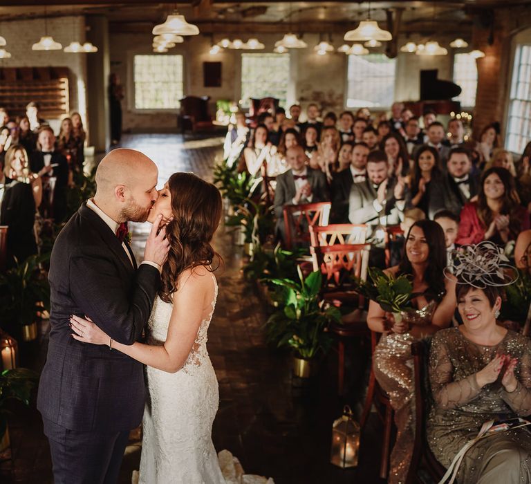 Bride in Martina Liana Lace Wedding Dress and Groom in Tom Ford Suit Kissing at the Altar