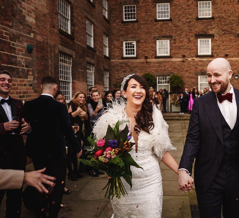 Bride in Martina Liana Wedding Dress &amp; Ostrich Feather Cover-up and  Groom in Tom Ford Suit Holding Hands