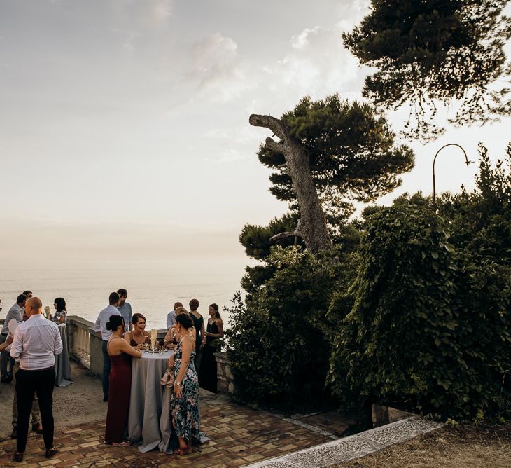 Guests enjoy drinks at destination wedding with sea views