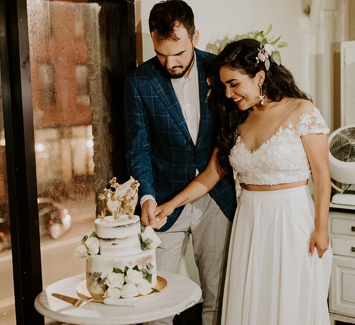 Bride and groom cut into semi naked wedding cake with dinosaur cake topper