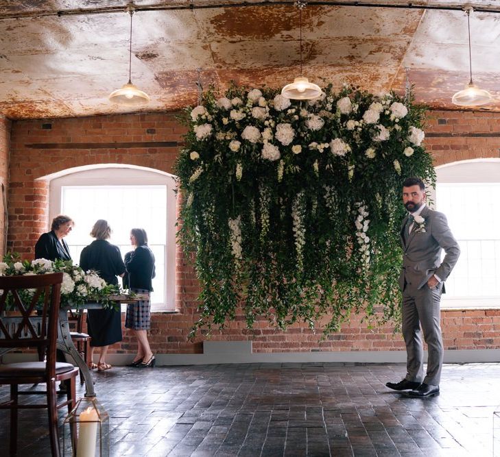 Groom waits in front of white flower installation