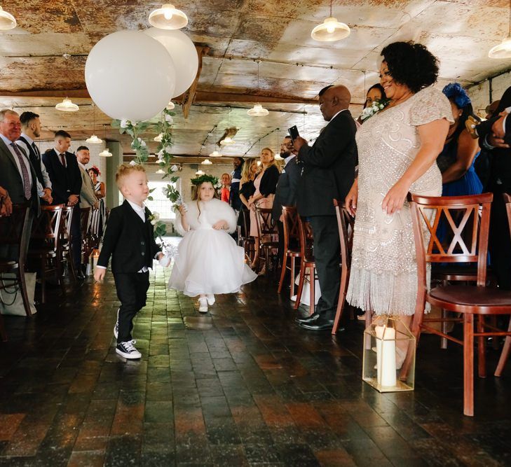 flower girl and page boy walk down the aisle with wedding balloons