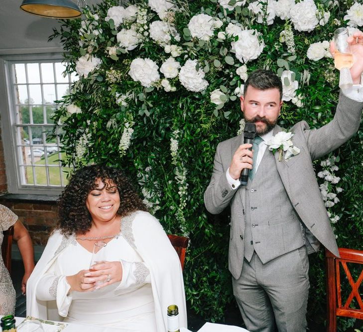 Groom makes wedding speech with floral backdrop