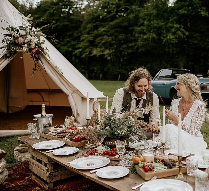 Bride and Groom Enjoying an Outdoor Grazing Table Next to a Bell Tent and Vintage Car