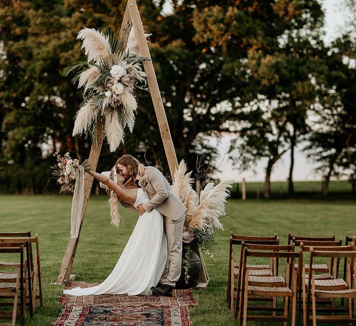 Bride and Groom Kissing at Wooden Frame Altar with Pampas Grass Floral Arrangement and Moroccan Rugs,