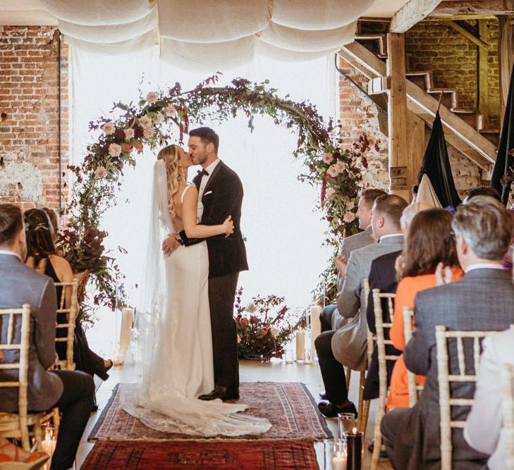 Bride and groom kiss in front of floral moon gate