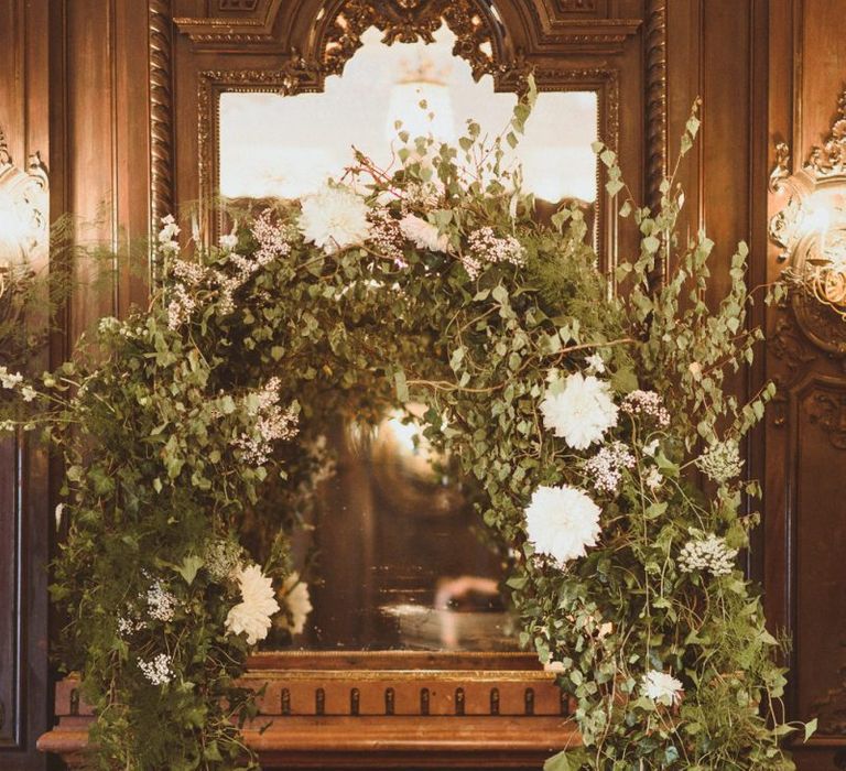 White floral and foliage archway with pillar candles and scattered petals