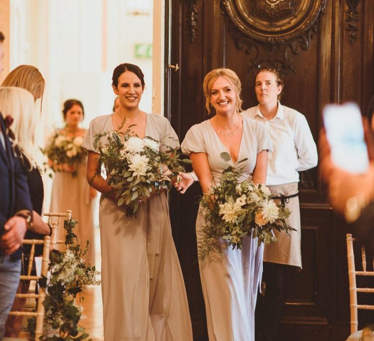 Bridesmaids wearing pale blue dresses walking down the aisle holding white foliage bouquets