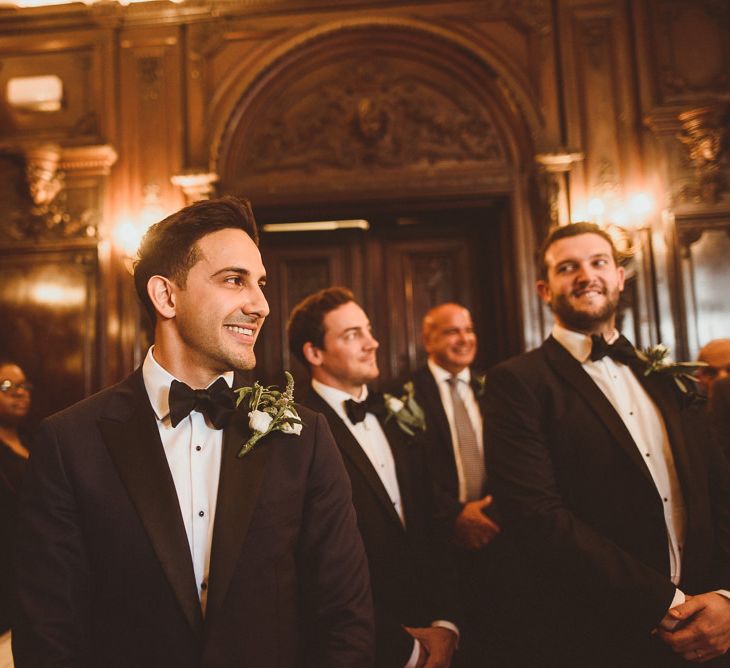 Groom wearing black tie and floral buttonhole waiting at the aisle