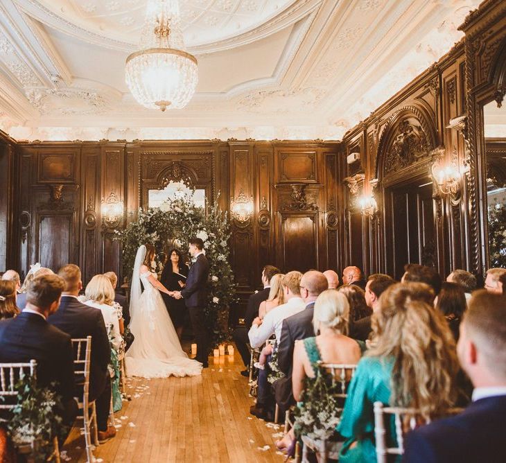 Bride and groom tie the knot at London ceremony with white foliage archway and floral chair back decor