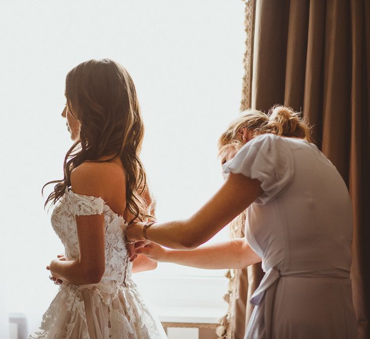 Bride getting into Martina Liana off the shoulder dress with laced details and tulle skirt