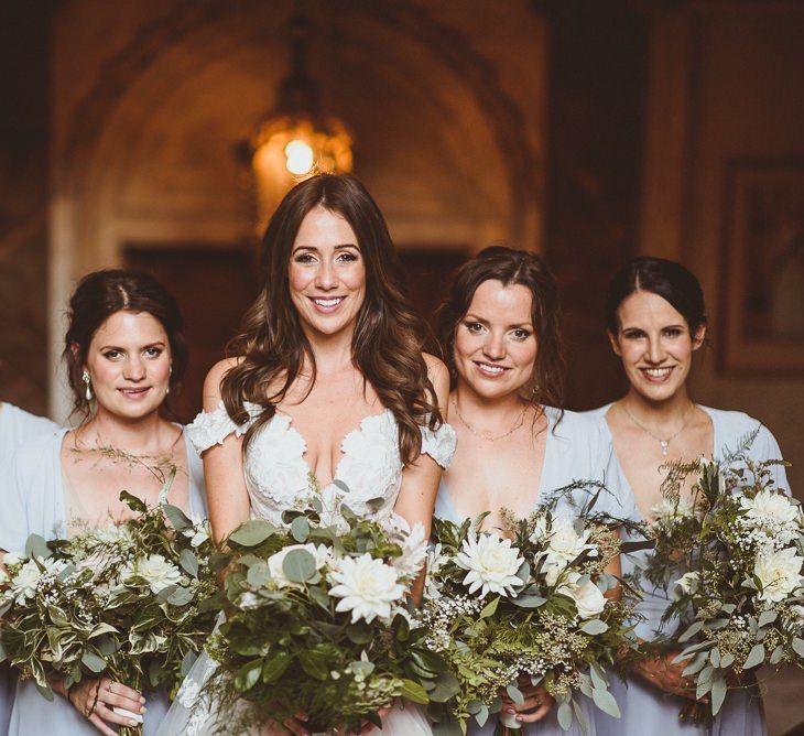 Bride wearing Martina Liana dress with her bridesmaids in pale blue dresses and white foliage bouquets