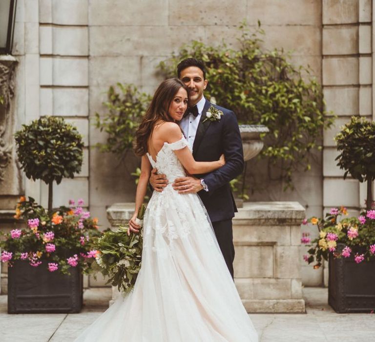 Bride wearing Martina Liana off the shoulder dress embraces with groom at London wedding