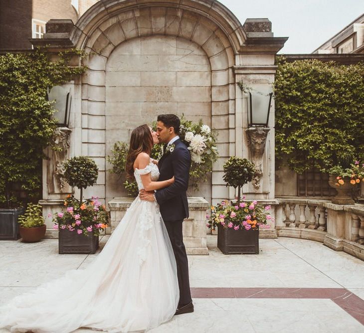 Bride wearing Martina Liana off the shoulder dress embraces with groom at London wedding