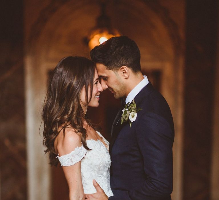 Bride clutching white foliage bouquet with groom wearing black tie and floral buttonhole