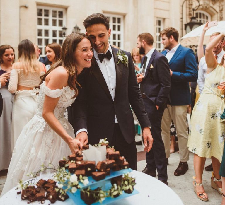 Bride and groom tuck into brownie tier wedding cake at outdoor drinks reception in London