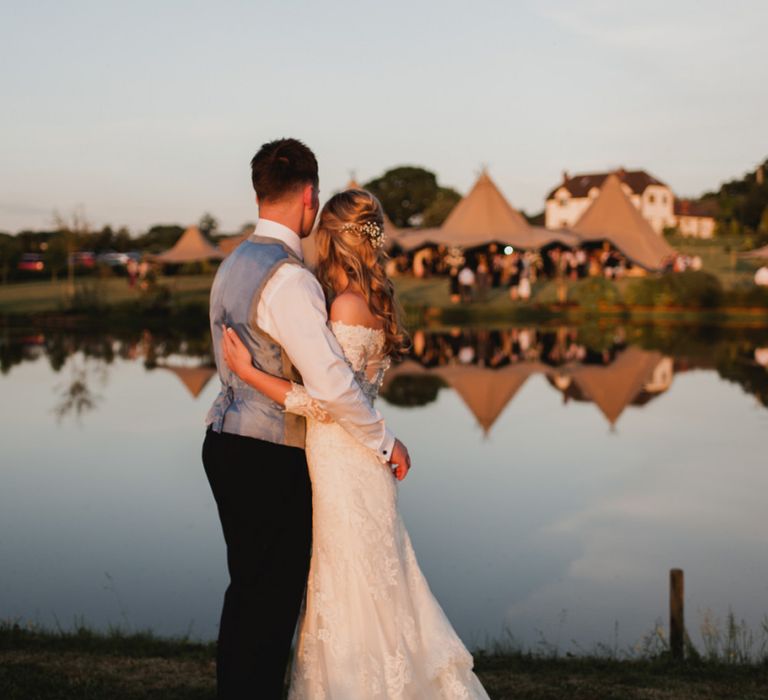 Bride in Lace Madeline Gardner Wedding Dress and Groom in TM Lewin Suit Embracing During Golden Hour